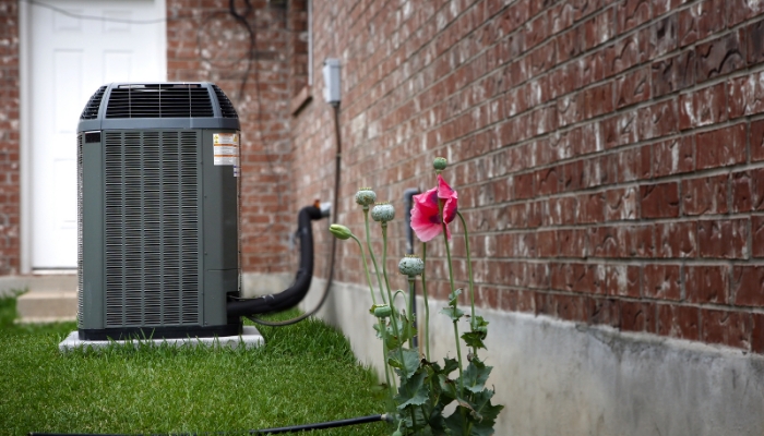 air conditioning unit installed outside a brick-walled home, with a blooming pink flower in the foreground